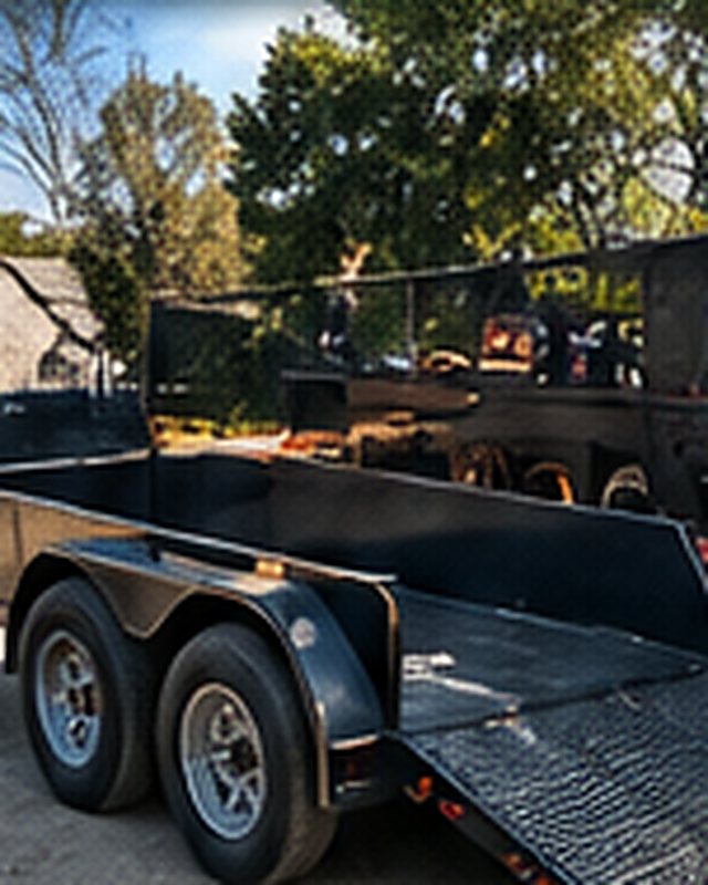 Black tandem-axle utility trailer with the rear ramp gate folded down.